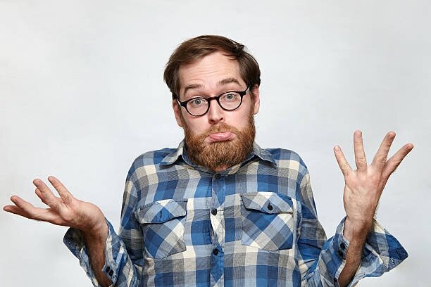 Man in checked shirt looking confused and making a 'what' gesture with his hands